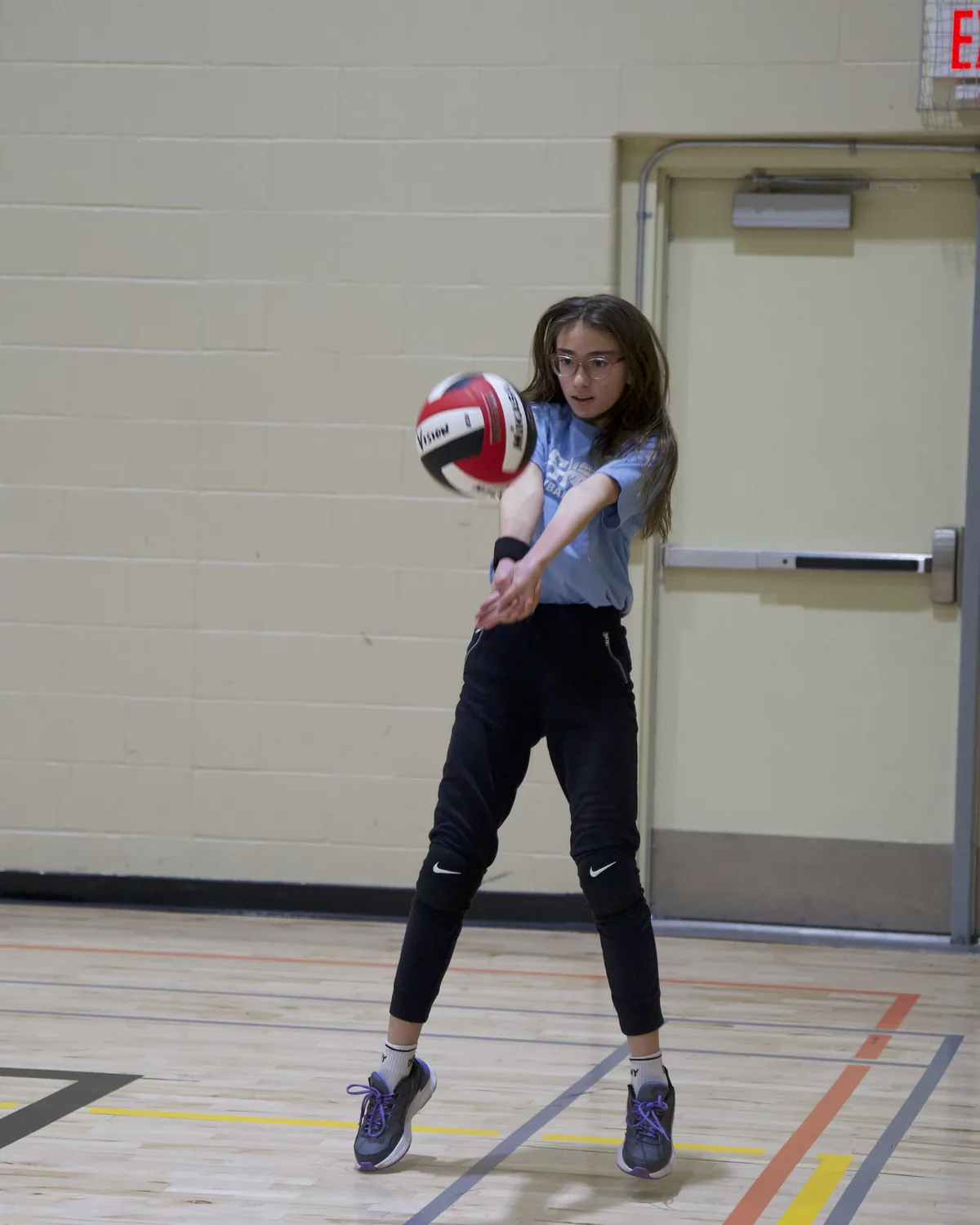 Youth volleyball player passing a ball in court shoes and knee pads